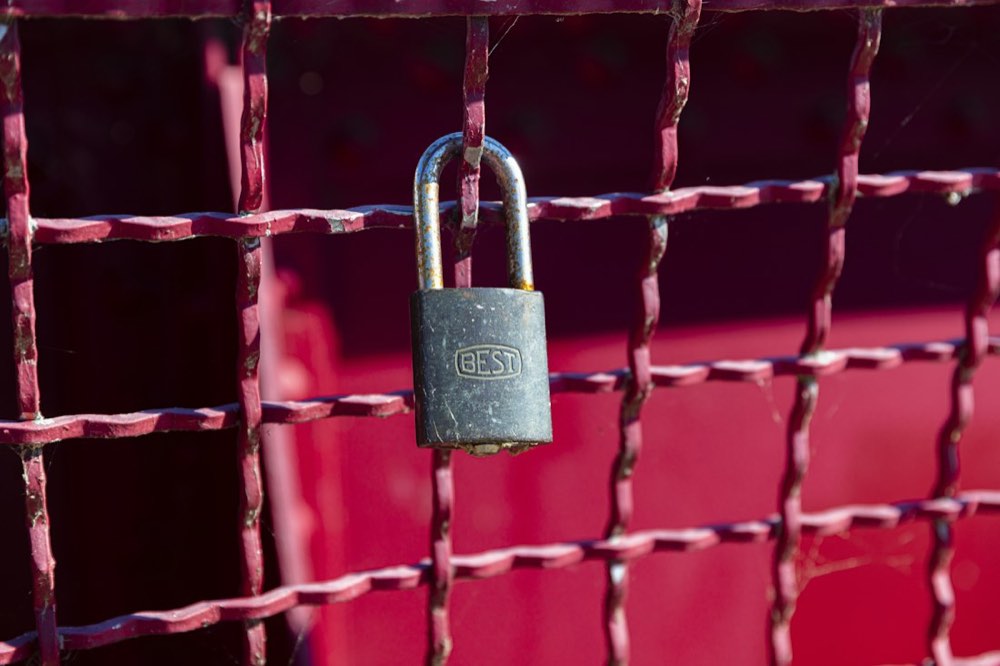 Brass padlock on a red metal gate
